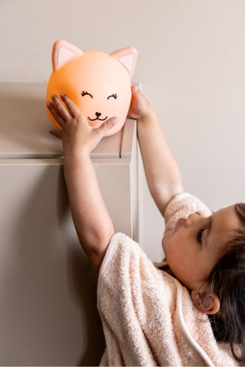 1. Child reaching for Trixie Baby's Mrs. Cat silicone night light on a shelf, providing a comforting glow