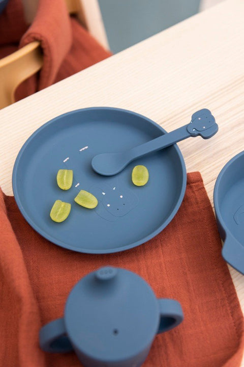 3. Close-up of Trixie Baby blue silicone plate with elephant spoon and green snacks on a wooden table