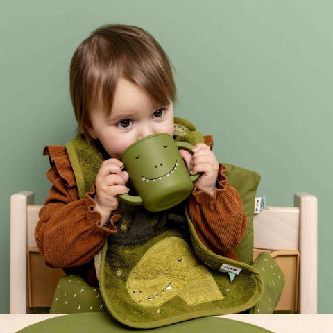 1. Toddler drinking from green dinosaur-themed silicone sippy cup at table