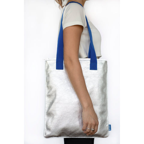 2. Woman wearing Daz Studio silver leather tote with blue straps, shown from the side