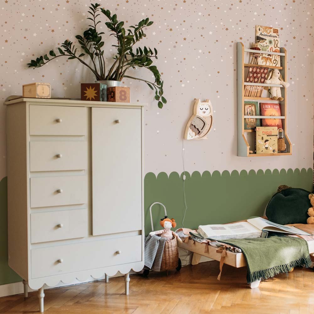 1. Children's room with powder pink star-patterned wallpaper by Dekornik, featuring a white dresser, green scalloped wall border, and wooden bookshelf