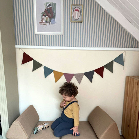 5. Child playing in a room with beige and blue striped wallpaper, colorful bunting, and framed art