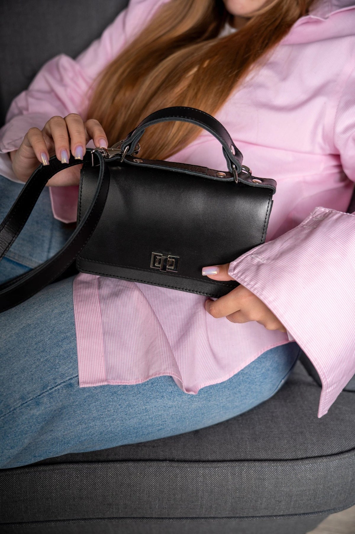 1. Woman holding Zelma Kraft black small briefcase handbag with adjustable strap, styled with pink blouse and jeans