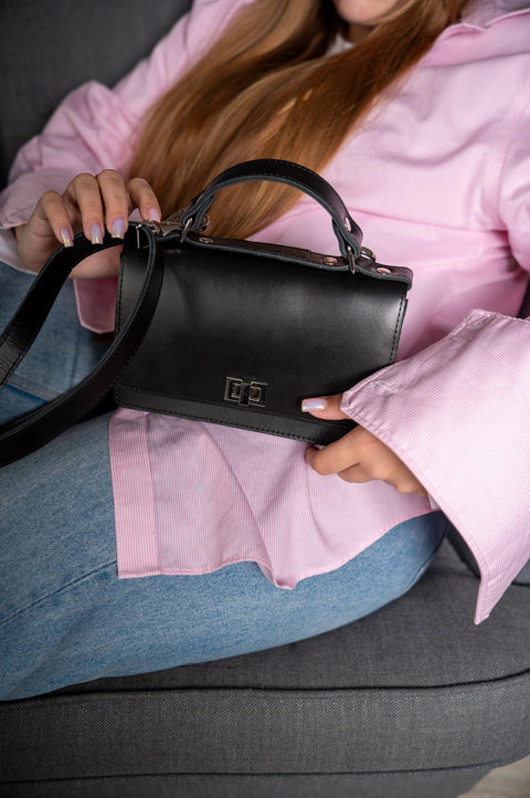 1. Woman holding Zelma Kraft black small briefcase handbag with adjustable strap, styled with pink blouse and jeans