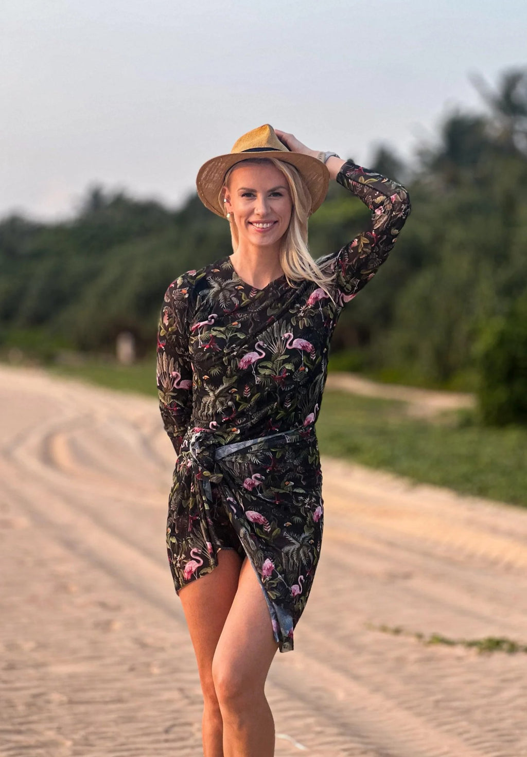 1. Woman wearing Smarttan Eeva Tropics Tan Through Long-Sleeve Shirt on beach, showcasing floral pattern and breathable fabric