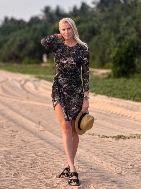 2. Woman in Smarttan Eeva Tropics Tan Through Long-Sleeve Shirt, holding hat, highlighting tan-through design and beach setting
