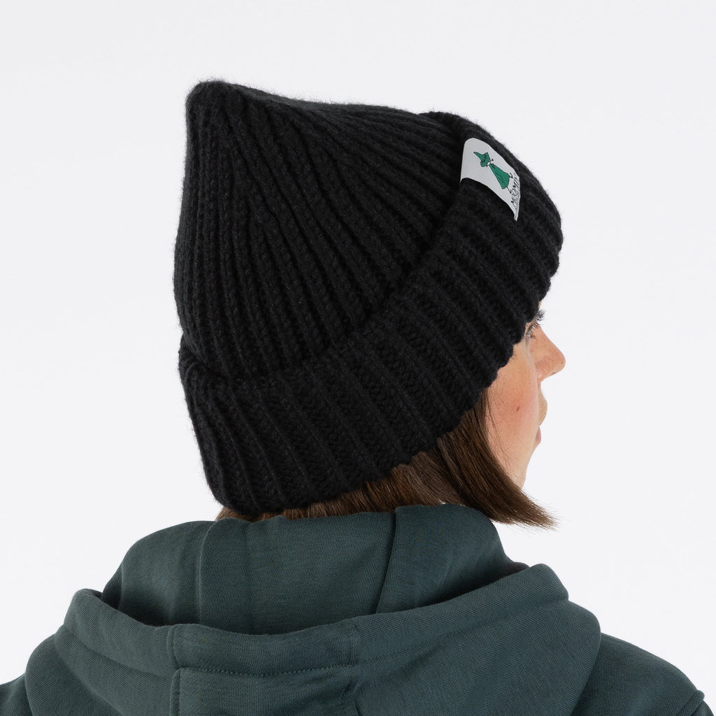1. Woman wearing black chunky beanie with Moomin by NordicBuddies logo, shown from side, white background