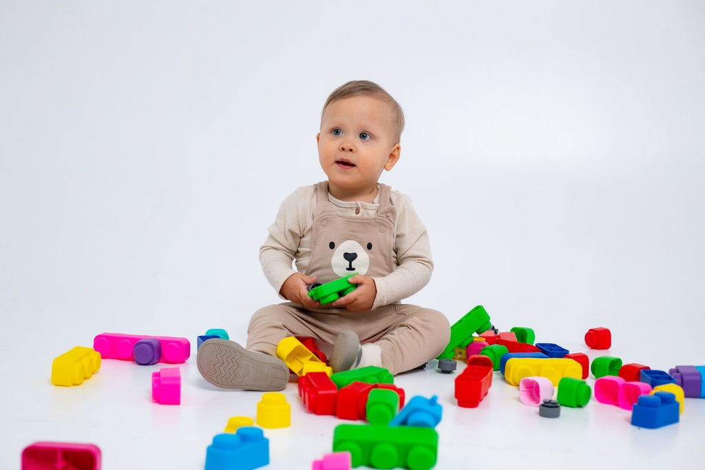 7. Baby in beige outfit sitting among colorful soft blocks on a white background