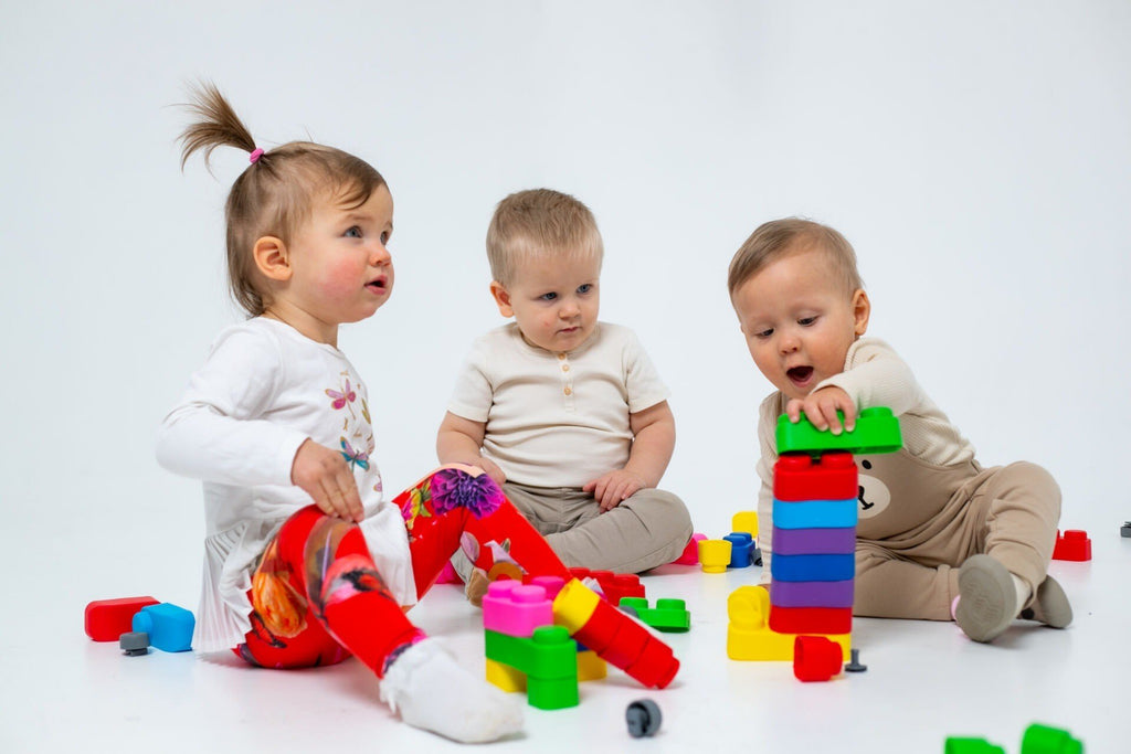 1. Three toddlers playing with colorful soft blocks on a white background, enhancing creativity and motor skills.