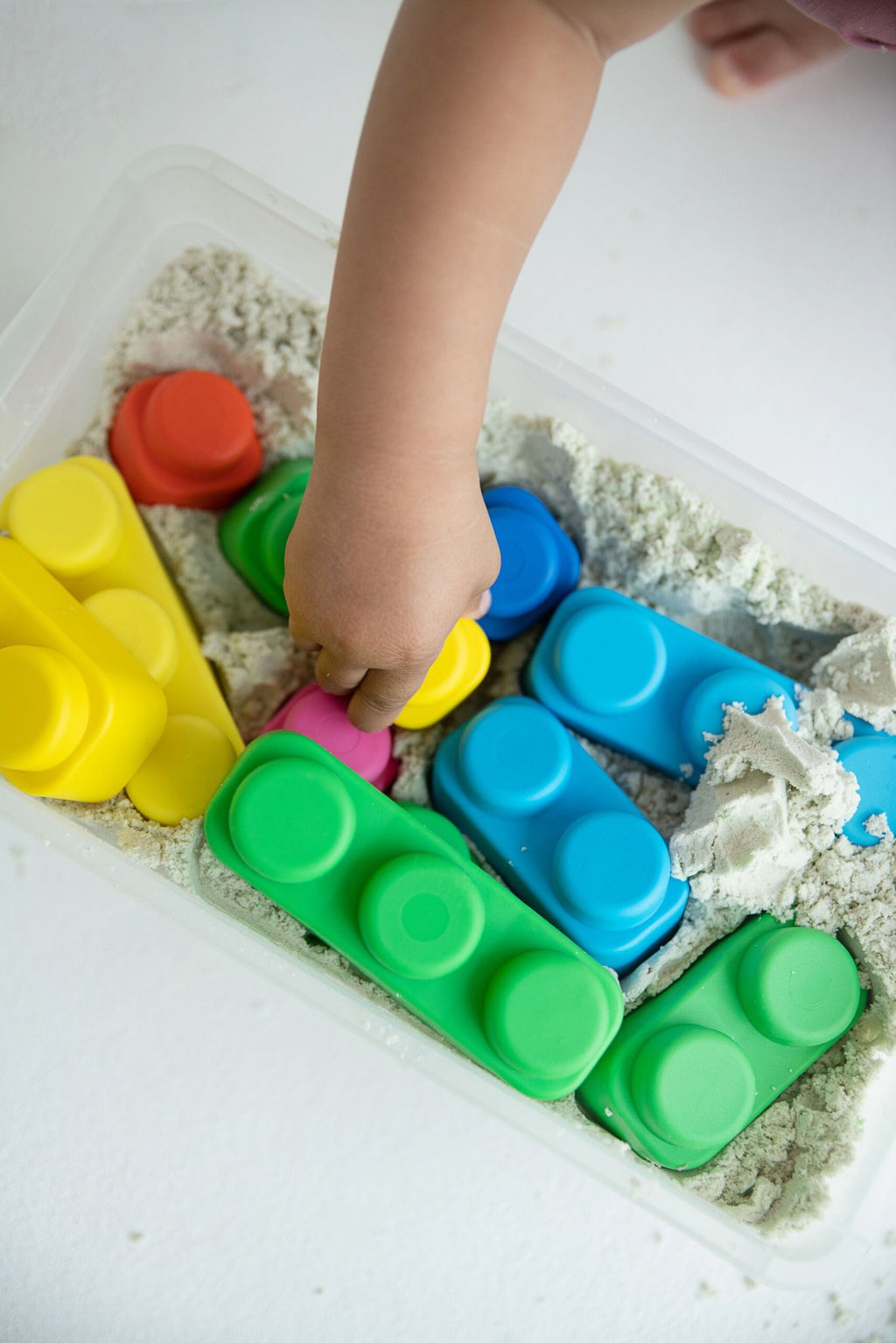 3. Close-up of toddler's hand reaching for colorful soft blocks in a sensory bin, enhancing tactile exploration.