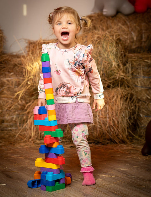 2. Young girl in pink outfit playing with a tall tower of colorful soft blocks in a rustic setting