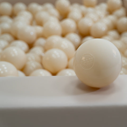 2. Single beige soft play ball with IGLU logo in focus, surrounded by more balls in a ball pit