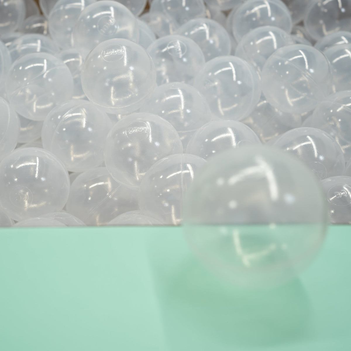 3. Group of translucent IGLU soft play ball pit balls on light green surface, showcasing quantity and texture