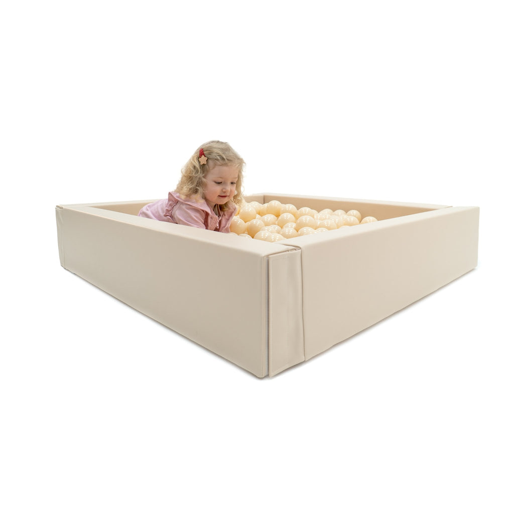 1. Child peeking over edge of beige IGLU soft play ball pit filled with cream-colored balls