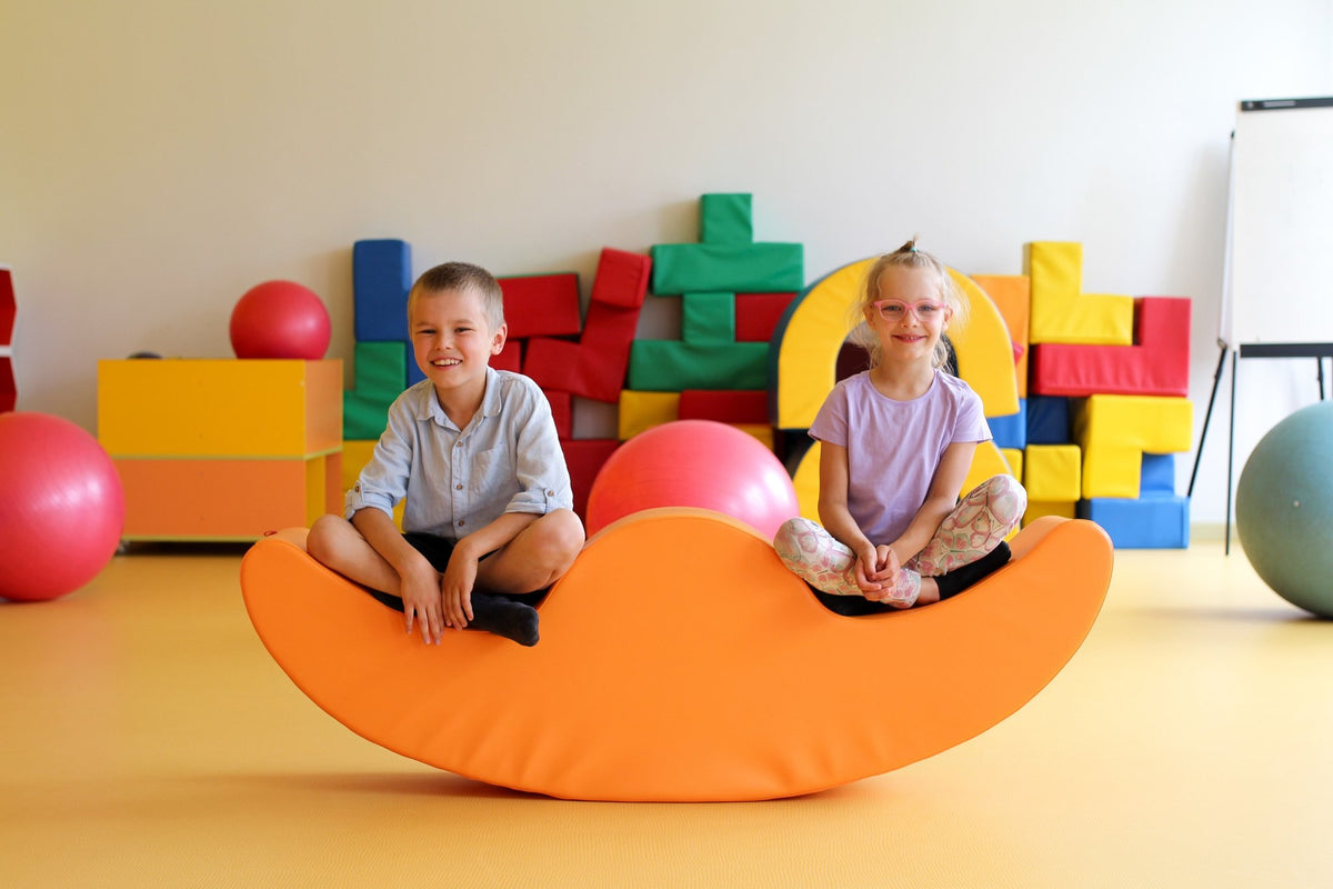 3. Boy and girl sitting on orange IGLU Soft Play Double Rocker Buddy in playroom with colorful blocks