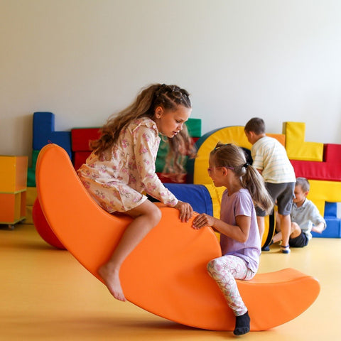 5. Two girls playing on orange IGLU Soft Play Double Rocker Buddy in playroom with colorful blocks