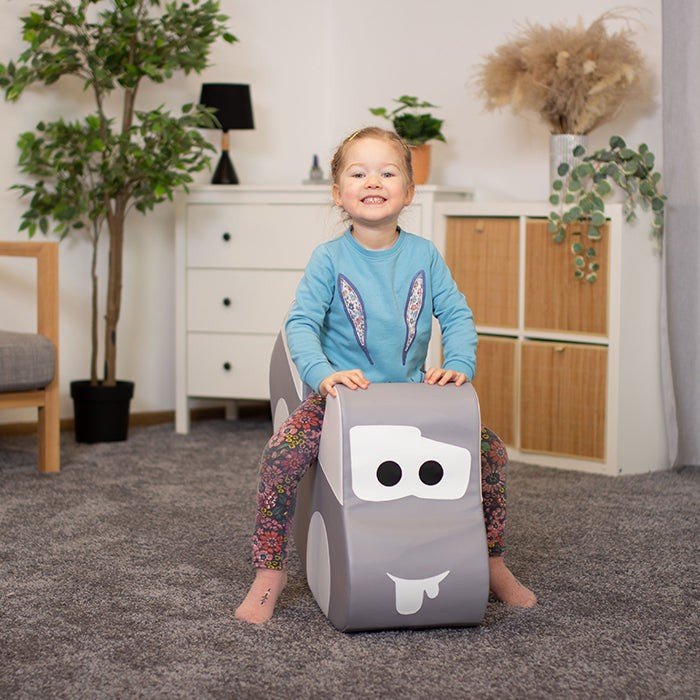 1. Smiling girl in blue top and floral leggings sitting on IGLU grey car-shaped soft play toy indoors, enjoying playtime