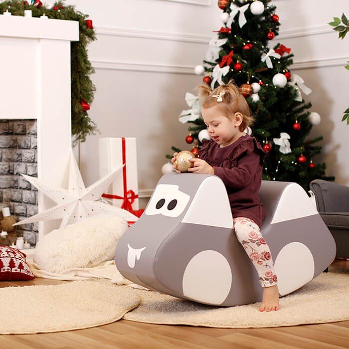 2. Child in maroon outfit playing on IGLU grey car-shaped soft play toy near Christmas tree, enhancing holiday fun