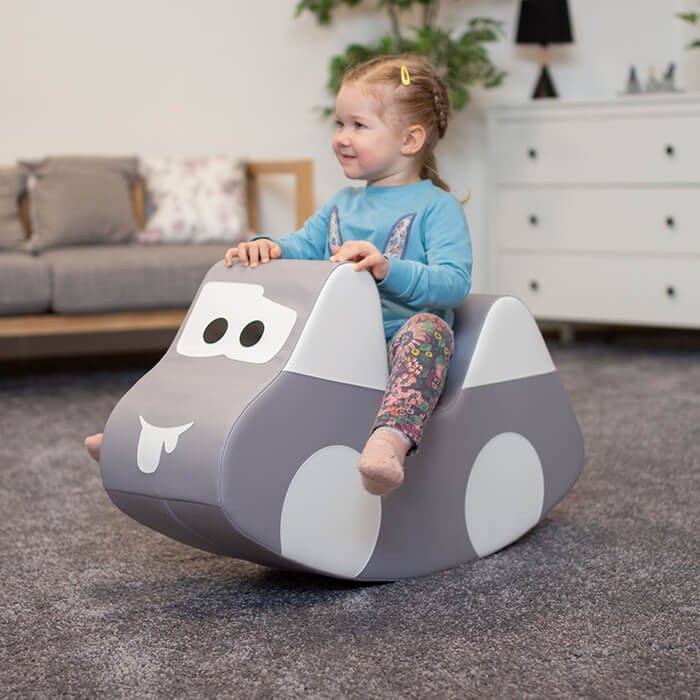 1. Young girl in blue top and floral leggings riding IGLU grey car-shaped soft play toy indoors, smiling and enjoying playtime