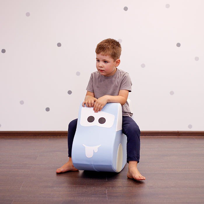 4. Boy sitting on light blue soft play ride-on toy car with cartoon face in room with polka dot wall