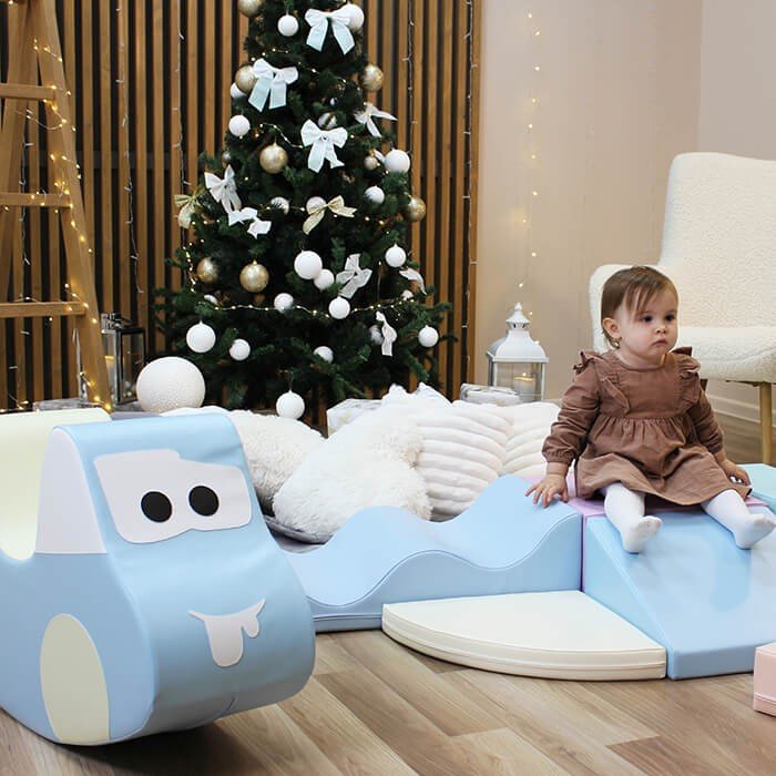 7. Toddler sitting on light blue soft play ride-on toy car next to Christmas tree and decorations