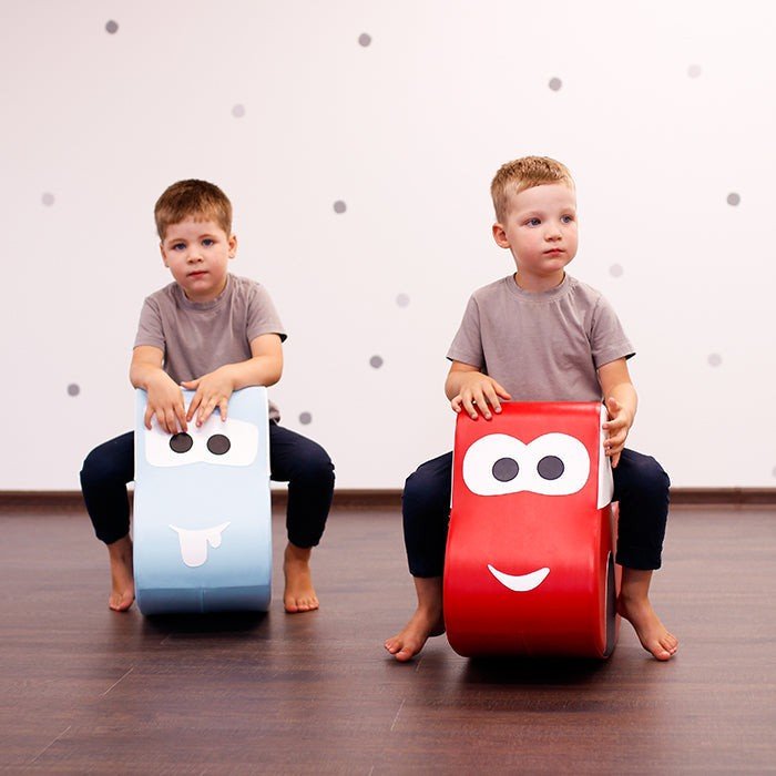 2. Two boys sitting on IGLU soft play ride-on toys, one red car and one blue car, in a playroom