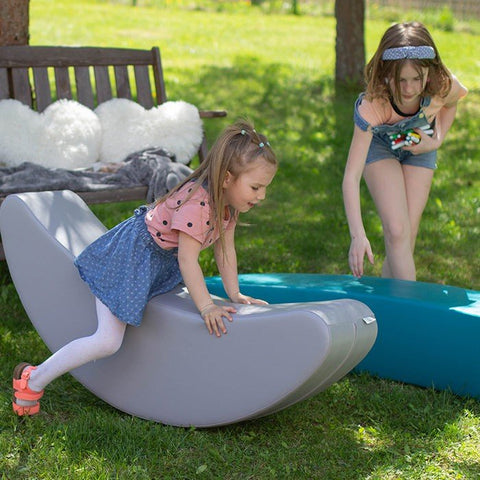 5. Two young girls playing on grey and blue banana-shaped rocking toys outdoors