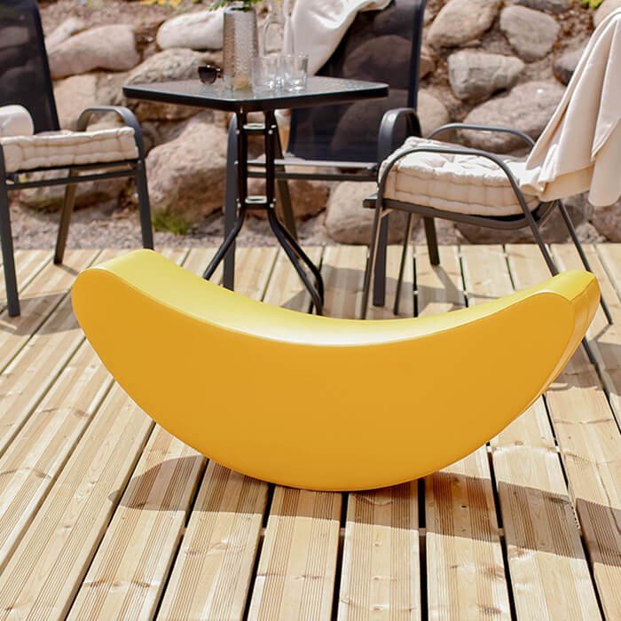 1. Yellow banana-shaped soft play rocking toy on wooden deck with outdoor seating in background