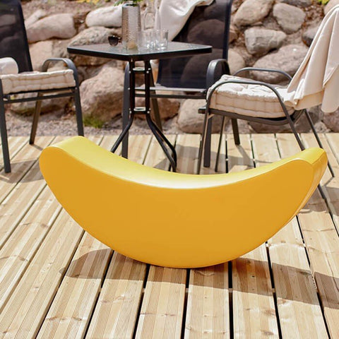 1. Yellow banana-shaped soft play rocking toy on wooden deck with outdoor seating in background