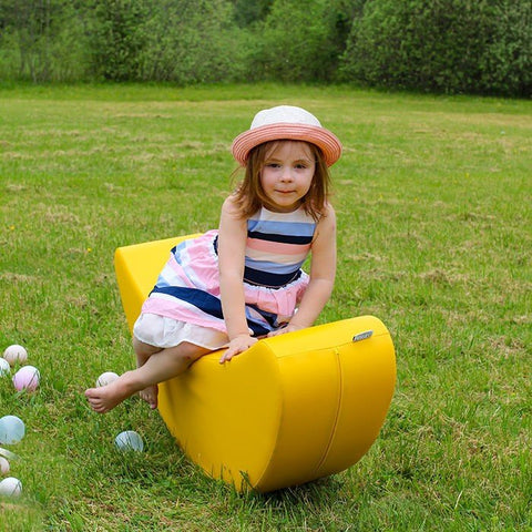 1. Young girl in striped dress and hat sitting on yellow banana-shaped rocking toy in grassy field
