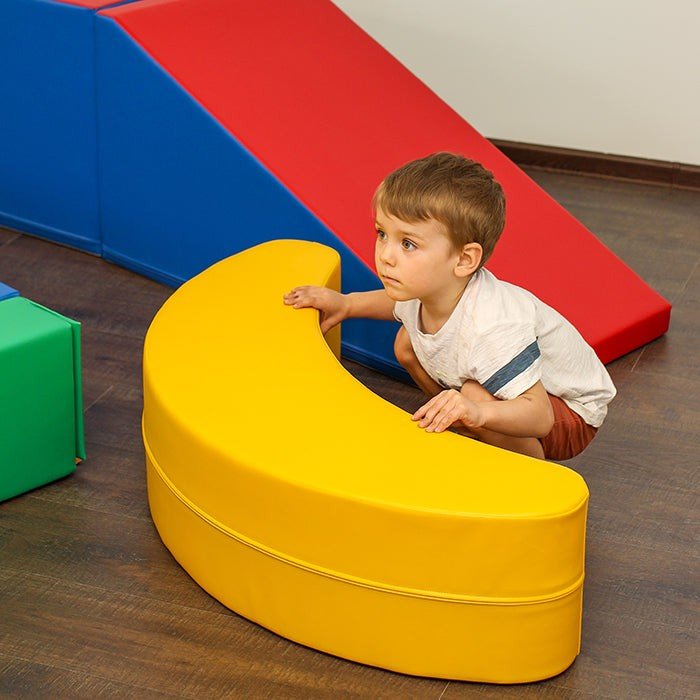 1. Young boy playing with yellow banana-shaped soft play toy in room with colorful play blocks