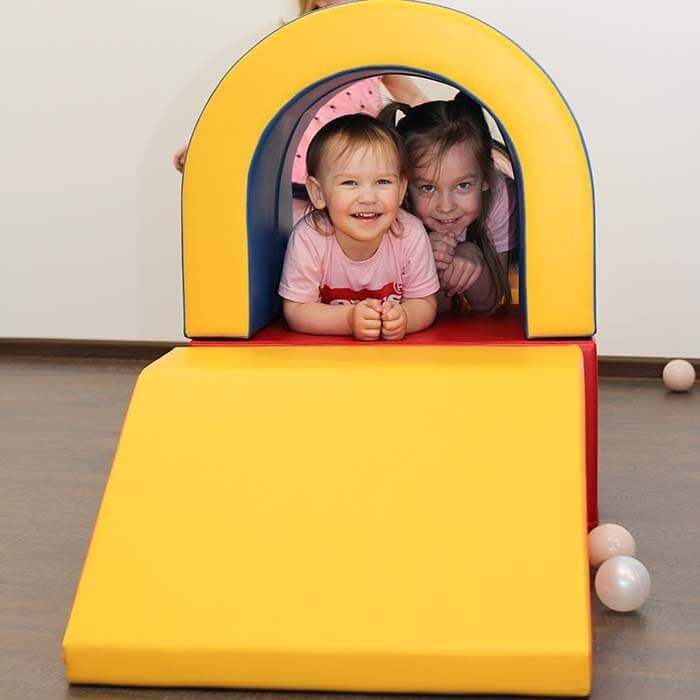 1. Two children smiling inside multicolor soft play tunnel set with yellow slide