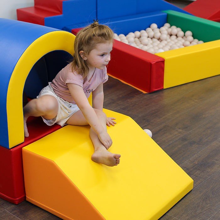 1. Young girl playing on multicolor soft play tunnel set with blue arch and yellow slide