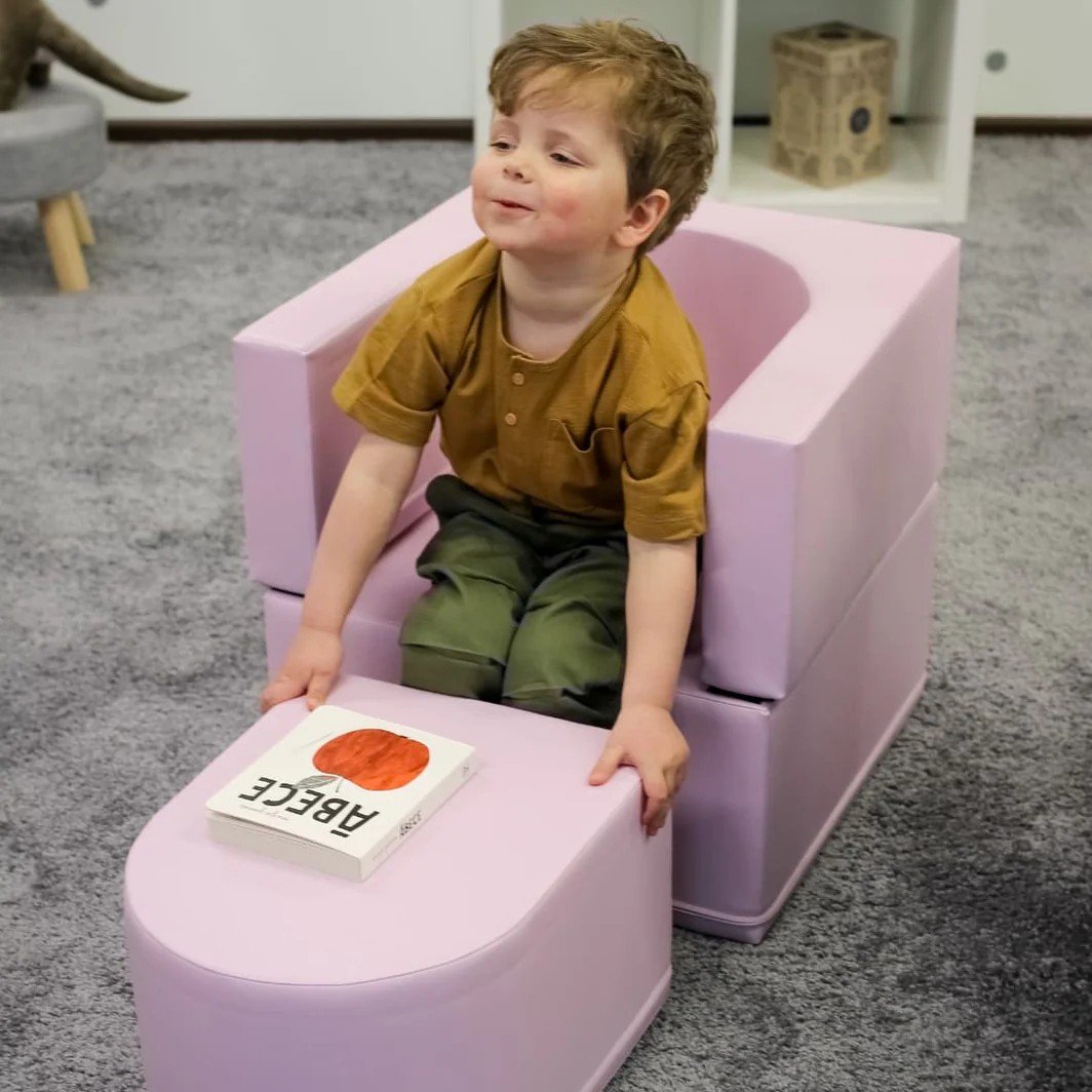 1. Child leaning on pink IGLU Snoozy soft play sofa chair with a book in a playroom