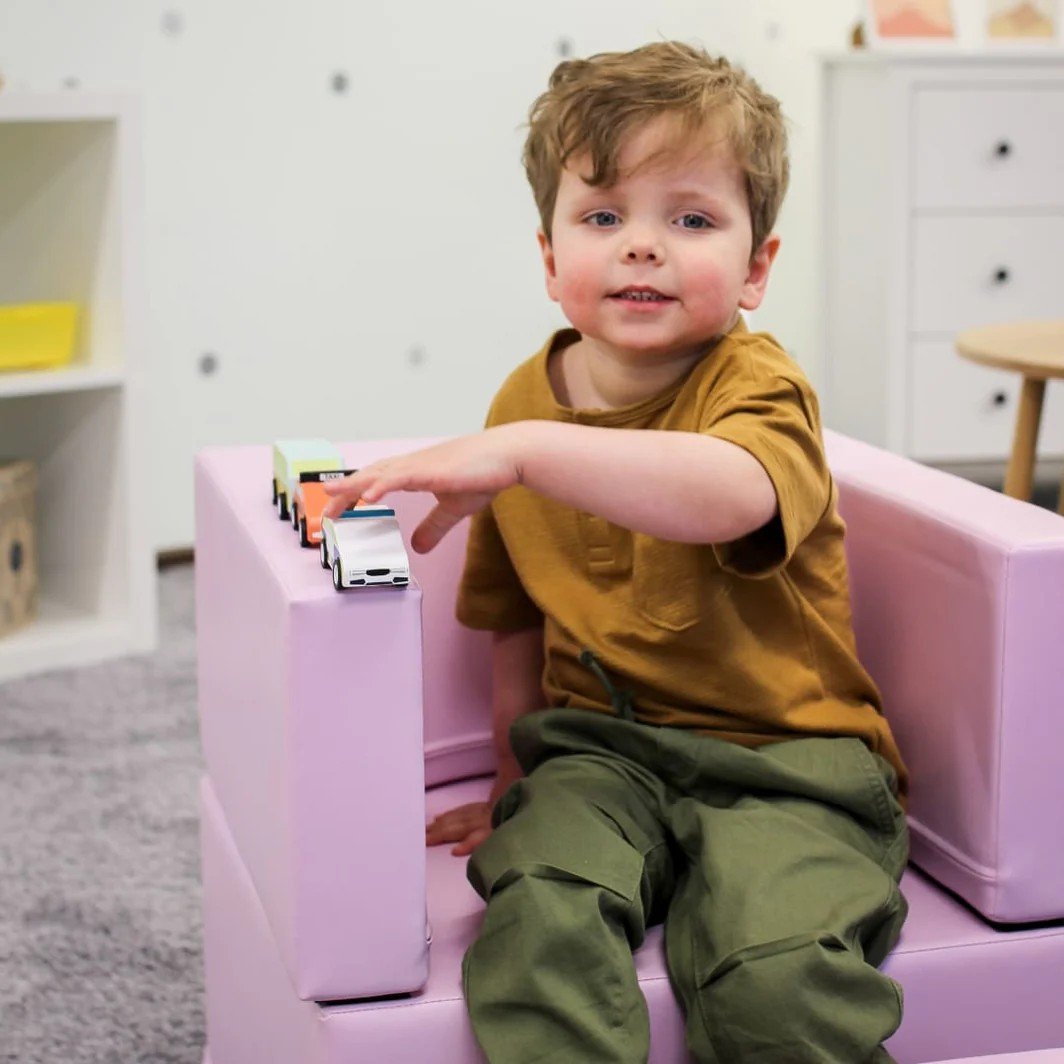 1. Child sitting on pink IGLU Snoozy soft play sofa chair playing with toy cars in a playroom
