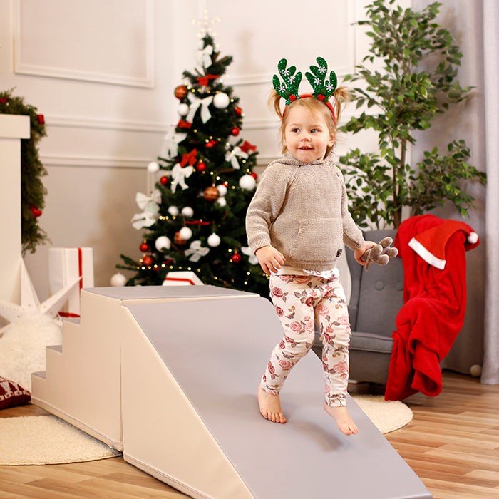 5. Child wearing reindeer antlers playing on beige and grey soft play slide in a festive living room