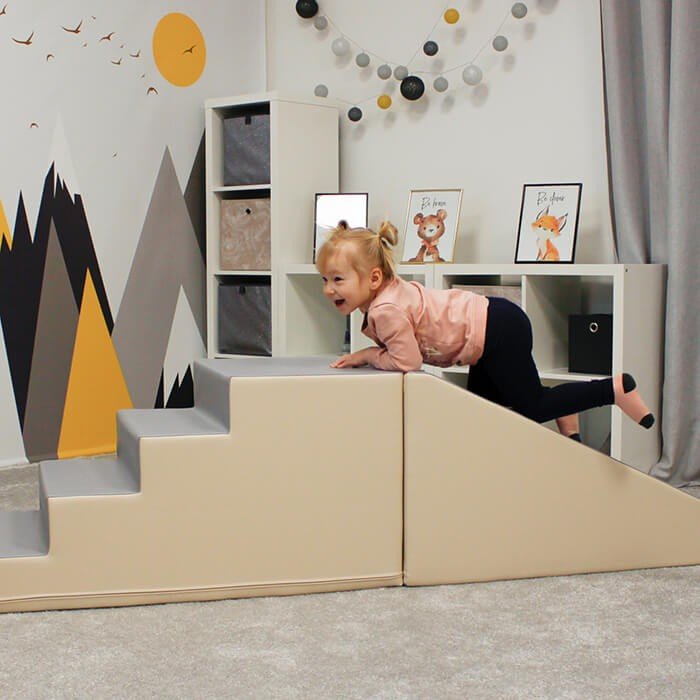 11. Child climbing beige and grey soft play steps in a playroom with decorative wall art