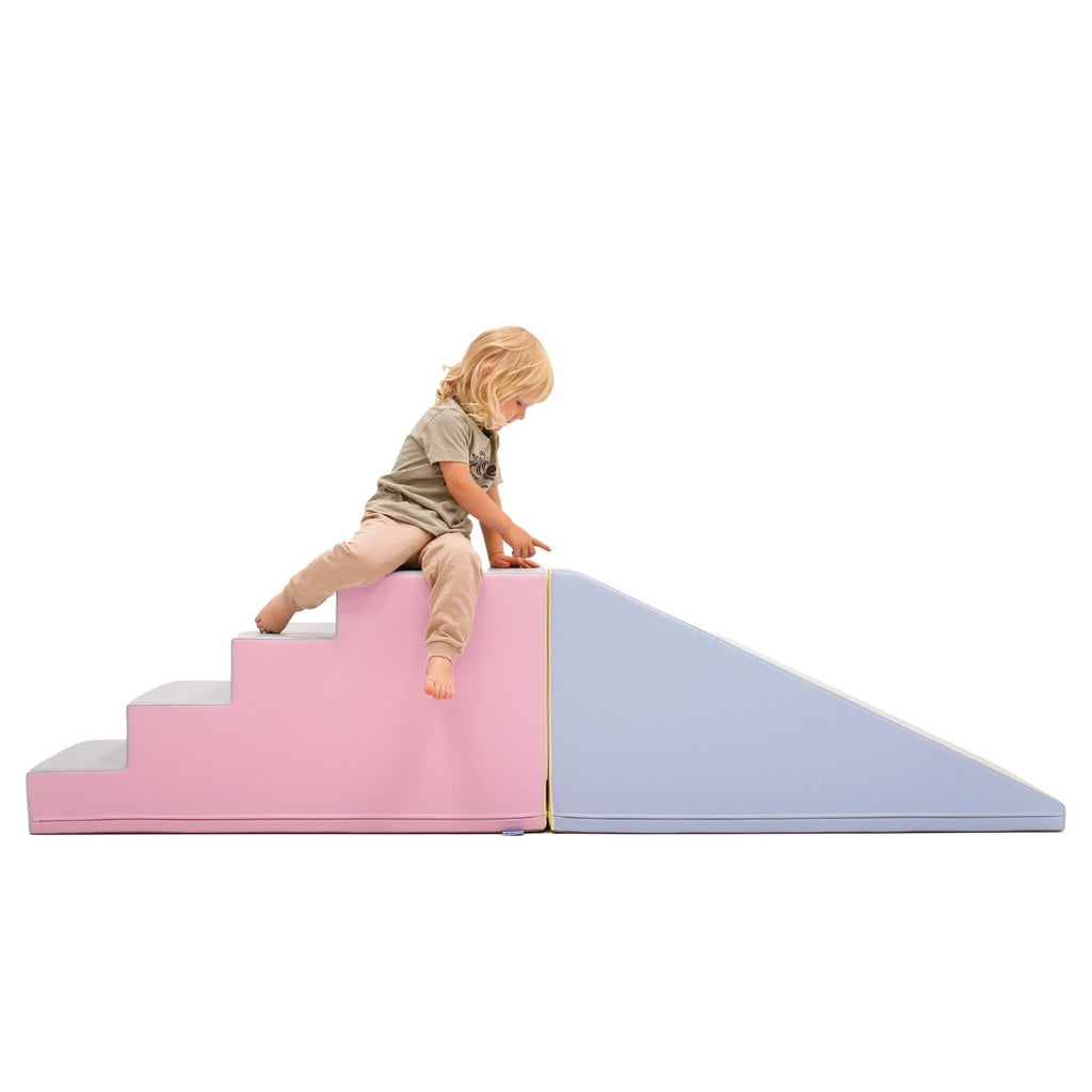 1. Child sitting on pastel pink and blue soft play step and slide set in a studio setting
