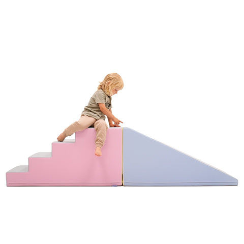 1. Child sitting on pastel pink and blue soft play step and slide set in a studio setting