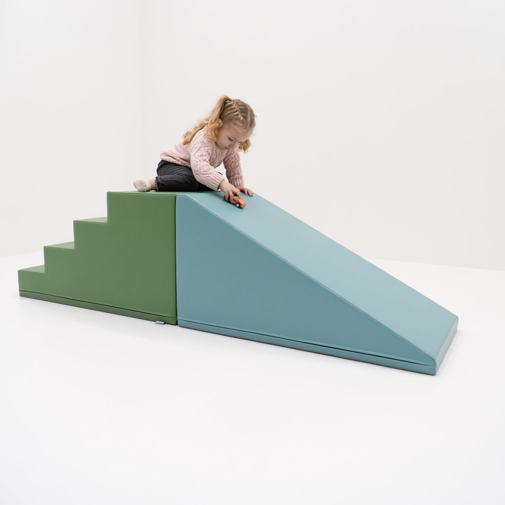 4. Young girl playing on IGLU soft play step and slide set in pastel turquoise and green, in a white room