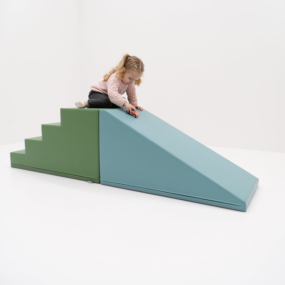 4. Young girl playing on IGLU soft play step and slide set in pastel turquoise and green, in a white room