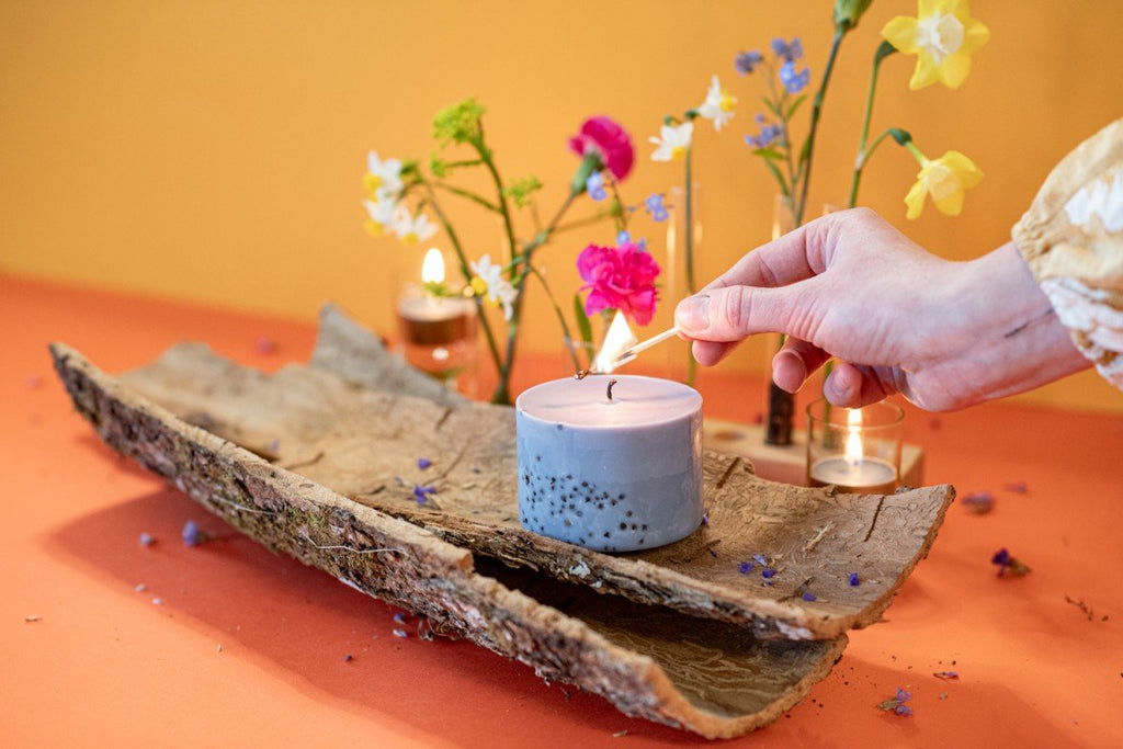 8. TL Candles hand-made soy wax candle with patchouli scent being lit, surrounded by colorful flowers