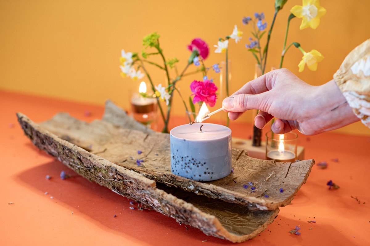 8. TL Candles hand-made soy wax candle with patchouli scent being lit, surrounded by colorful flowers