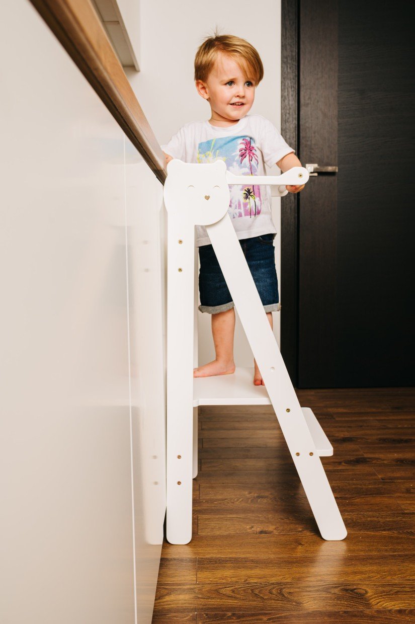 18. Child standing on white step stool in kitchen