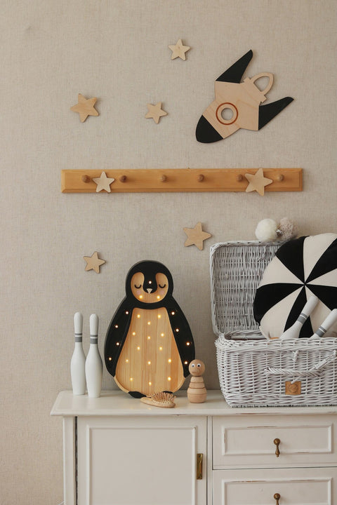 4. Beige wall with wooden rocket and stars above cabinet with penguin lamp and toys