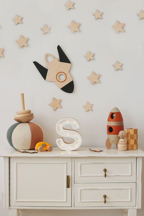 1. Children's room with wooden rocket and stars wall decoration above white cabinet with toys