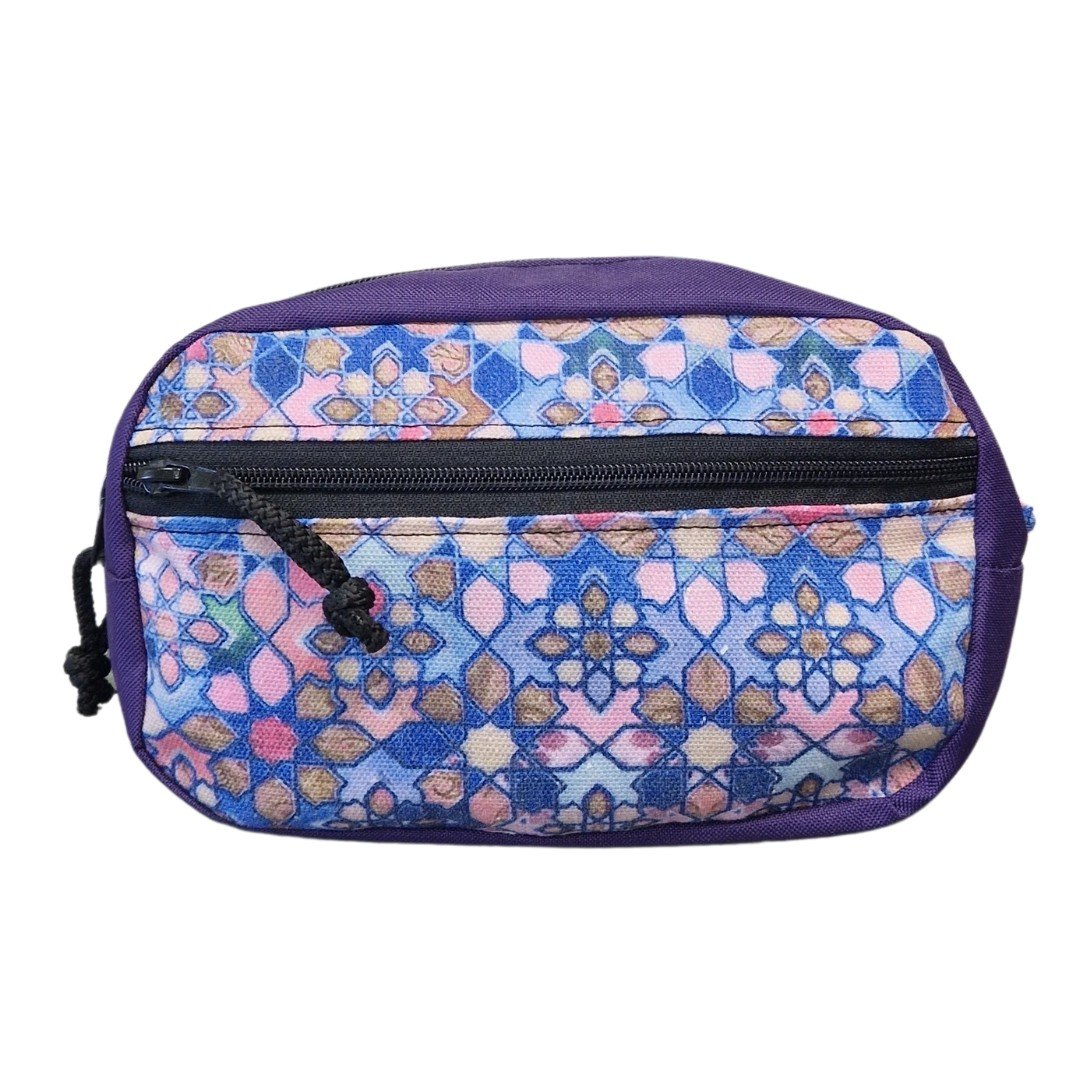 2. Front view of Drinbags waist bag with purple and multicolor geometric pattern, black zipper, studio background