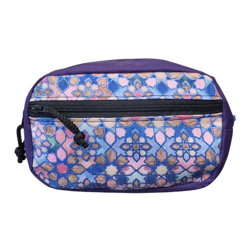 2. Front view of Drinbags waist bag with purple and multicolor geometric pattern, black zipper, studio background