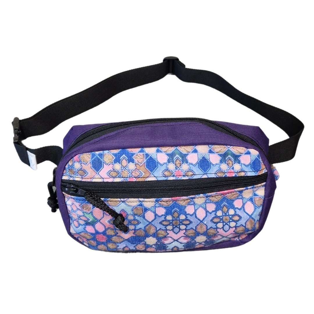 2. Drinbags water-resistant waist bag with purple and multicolor geometric pattern, adjustable black strap, studio background