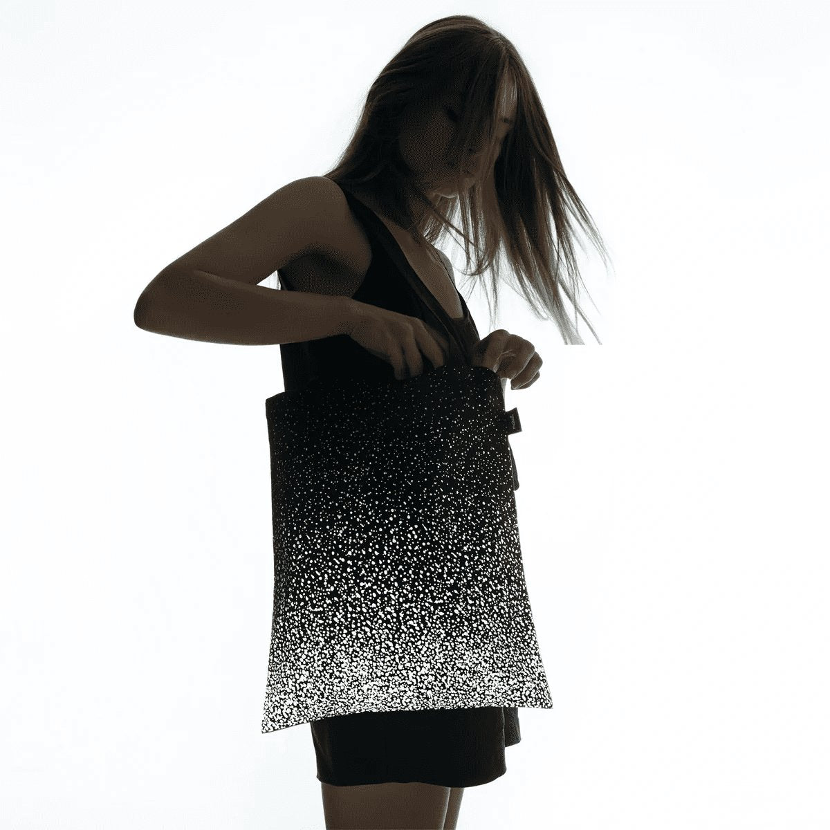 1. Woman holding MARCH Reflective Tote SPLASH in lifestyle setting, showcasing reflective design